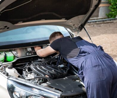 Professional mechanic at Homerton Car Repairs in Hackney E9 inspecting a vehicle underside for winter corrosion with a torch, workshop environment visible.